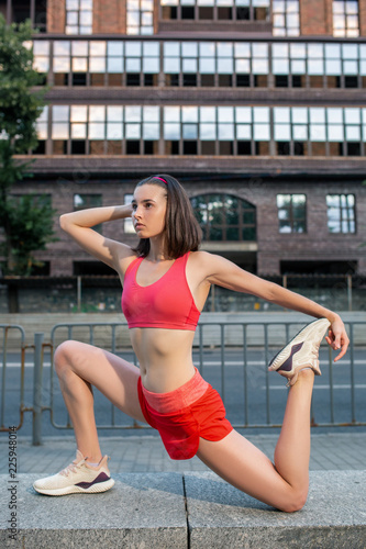 Fototapeta Naklejka Na Ścianę i Meble -  Sporty woman stretching and warming up legs before running urban fitness workout. Sport and healthy lifestyle concept.