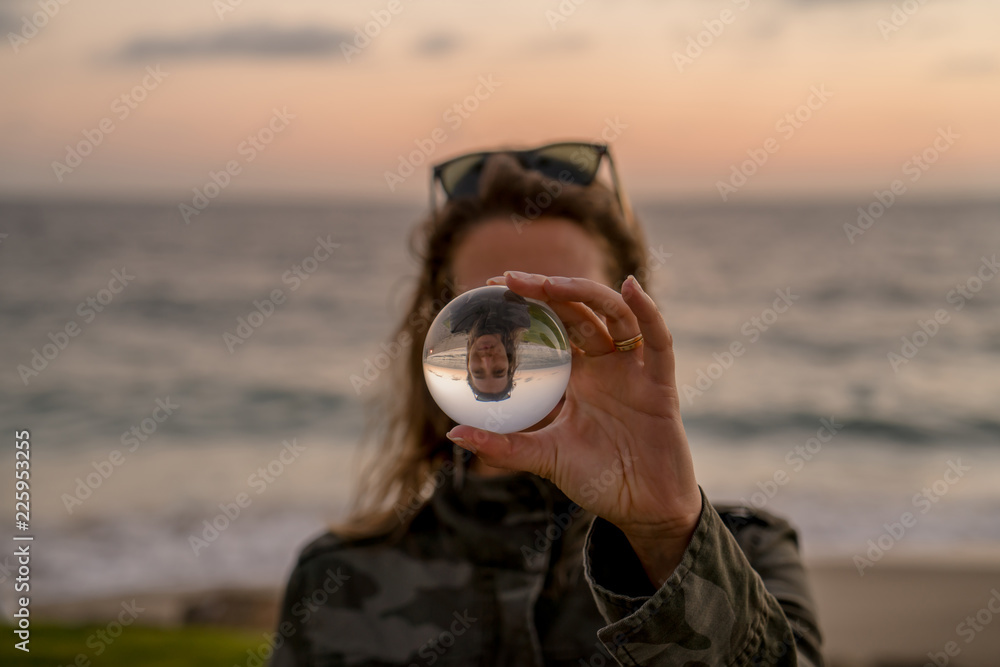 Fototapeta premium Girl holding a lens ball on the beach at sunset time