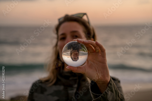 Girl holding a lens ball on the beach at sunset time