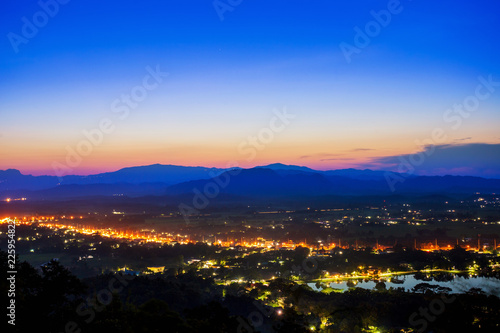 Aerial view at Doi Khao Kwai during blue zone after sunset. Mountain range as background with light tail on main road at Chiangrai city and big pond as foreground
