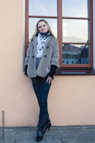 Full Length Portrait of Tranquil Caucasian Female in Light Coat in Front of the Window in The City.