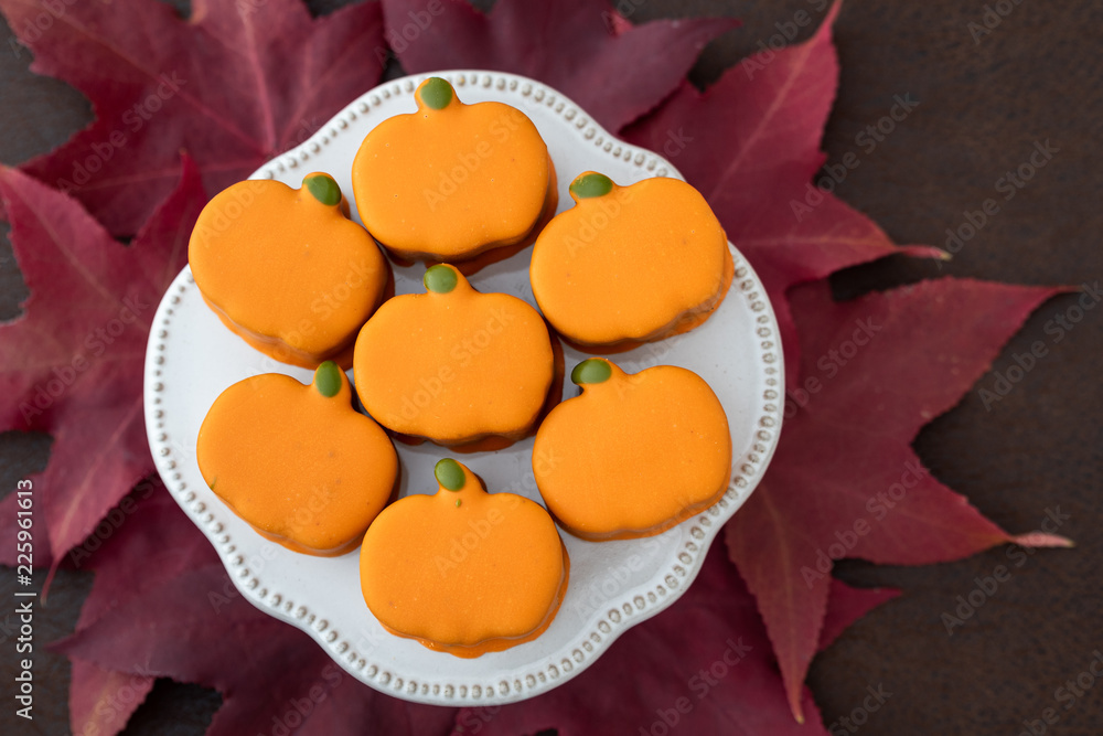White platter with small orange frosted pumpkin cakes on brown background, with red fall leaves

