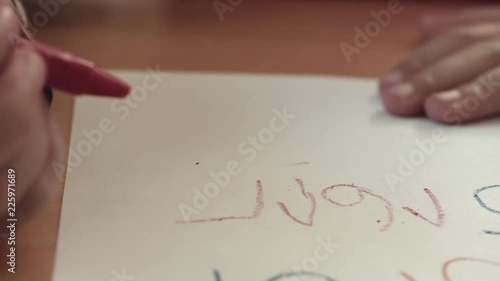 A child writes numbers with a red crayon as the camera tracks left. photo