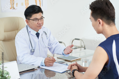Doctor listening to complaints of young patient and taking notes in his medical history