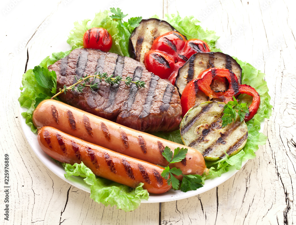 Grilled meat and vegetables over green leaves on white plate on the wooden table. Grilled meat and vegetables over green leaves on white plate on the wooden table.