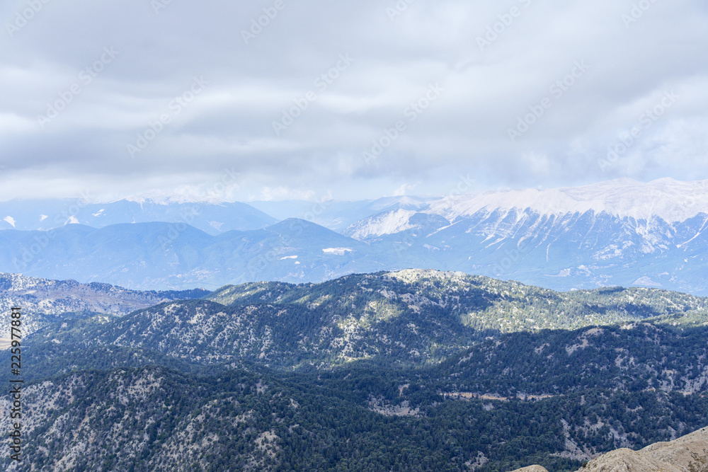 View from the Peak of Tahtali Mountain or Olympus to the tops of the Taurus Mountains, against the background of the cloud and the blue sky