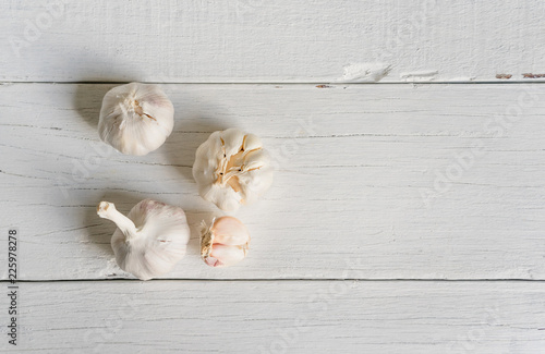 Organic garlic whole and cloves on white wood background.