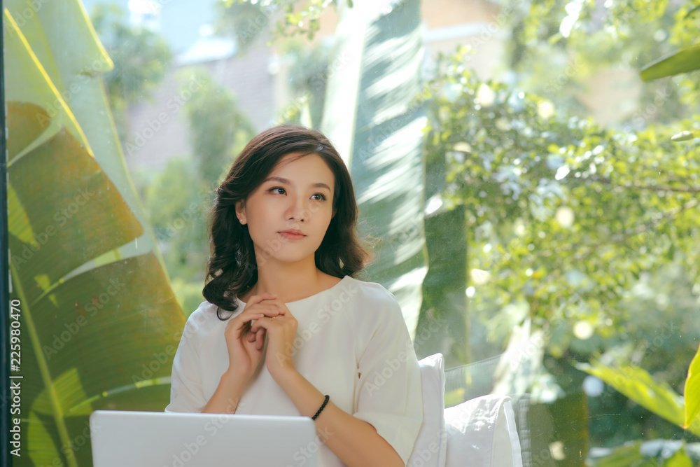 Portrait of young woman working holding laptop against panoramic window with garden view Portrait of young woman working holding laptop against panoramic window with garden view