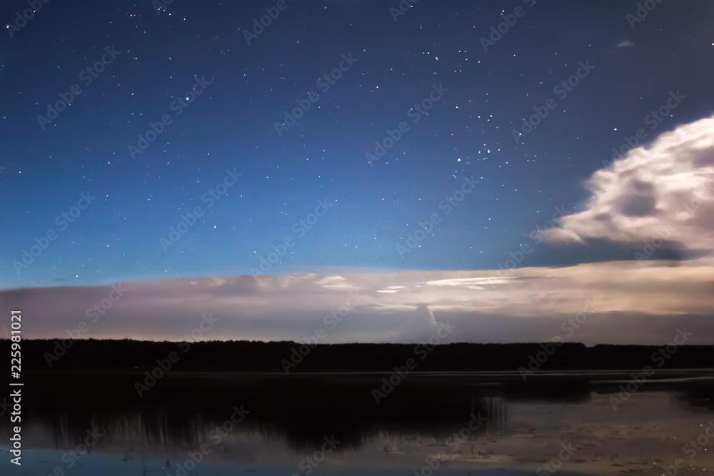 Naklejka premium Clouds and stars above lake in the summer night before thunder