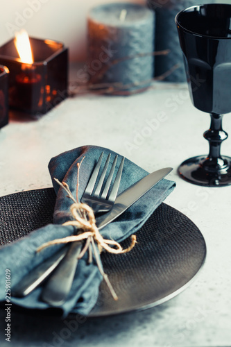 Festive table setting in a black style among black candles on a white table. Plate with fork and knife on a linen napkin. Thanksgiving or Halloween dinner. photo