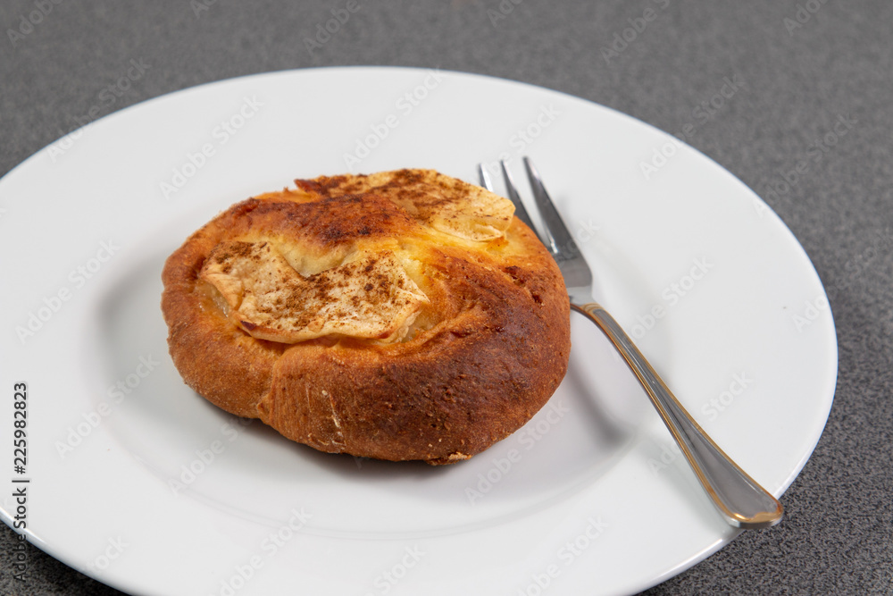 Single small bun beside a silver small fork on a white plate Single small bun beside a silver small fork on a white plate