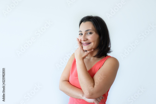 Portrait of happy attractive Caucasian woman holding chin and smiling. Pretty middle aged woman in pink dress coming up with idea. Bright idea concept.