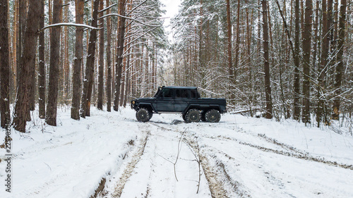 View on SUV 6x6 that rides by winter road in snow-covered forest