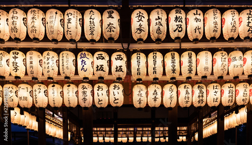 A row of lit lanterns hanging from a roof of a japanese temple