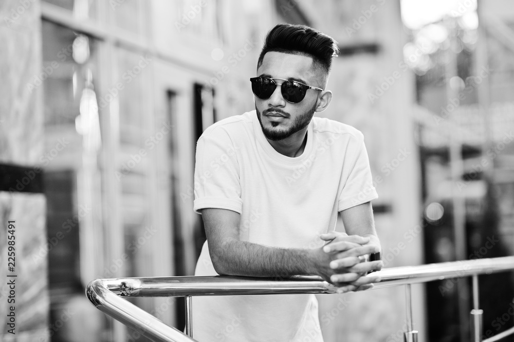 Stylish indian beard man at sunglasses and pink t-shirt. India model posed outdoor at streets of city.