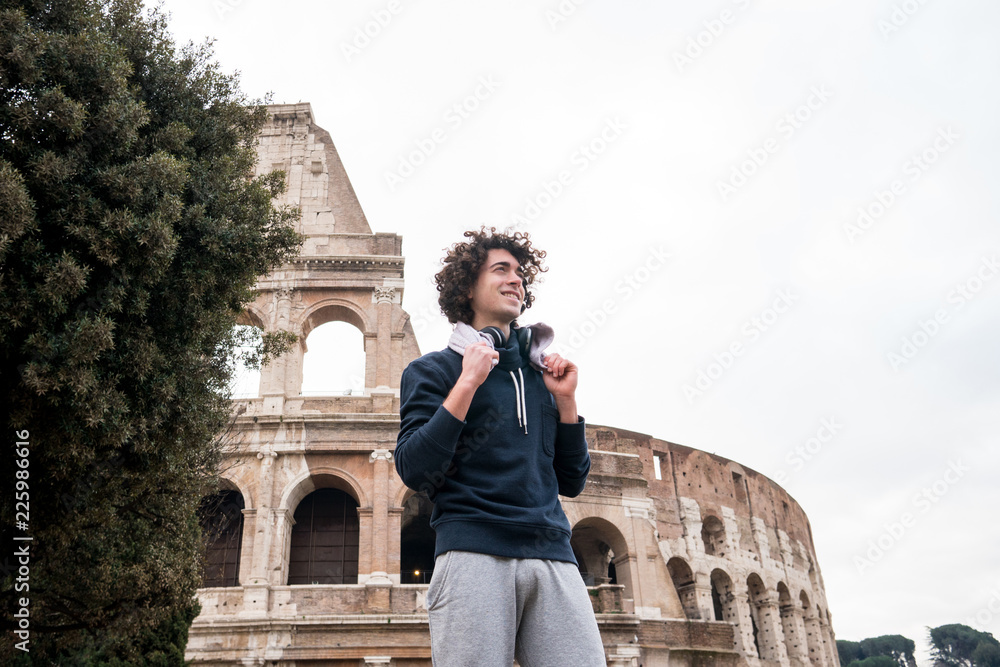 Handsome young sportsman relaxing after training with a towel around his neck in front of Colosseum in Rome
