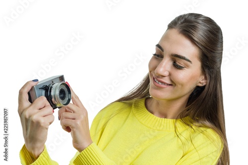 Beautiful young woman in yellow sweater holding vintage camera in her hands, smiling, taking pictures, looking with interest. White background isolated