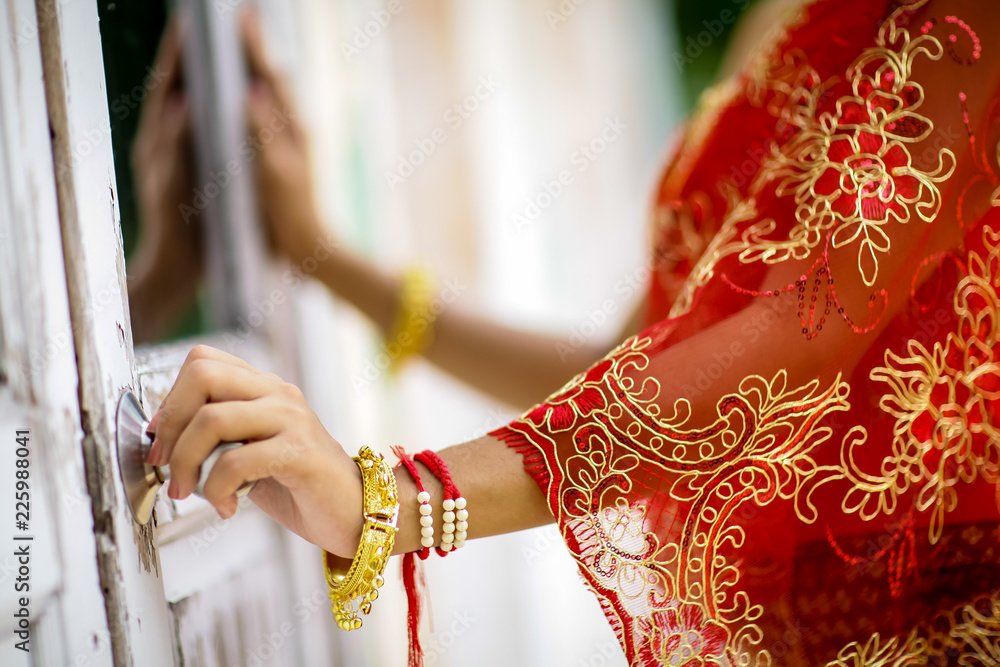 Close up bride’s hand wears thai traditional wedding dress, red lace fabric and ancient gold bracelet. No face. Thai traditonal wedding clothes.