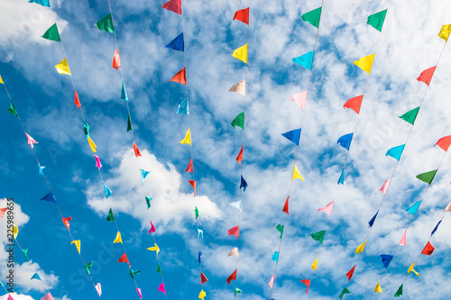 Multi-colored flags against a blue sky with clouds and a dome of a church.