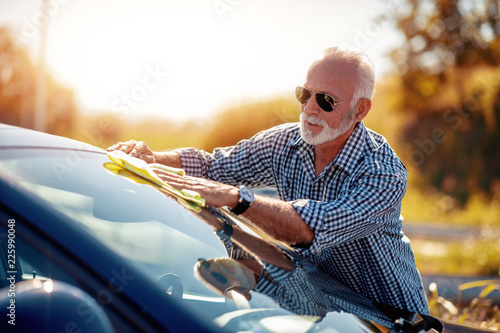 Portrait of smiling senior man cleaning his car