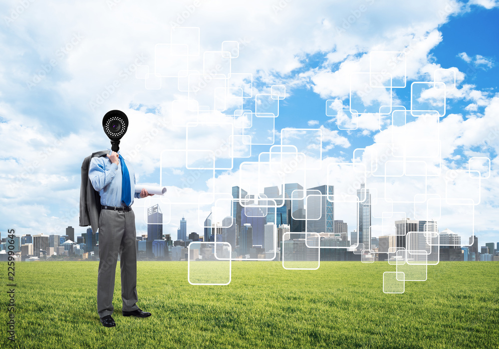 Camera headed man standing on green grass against modern cityscape