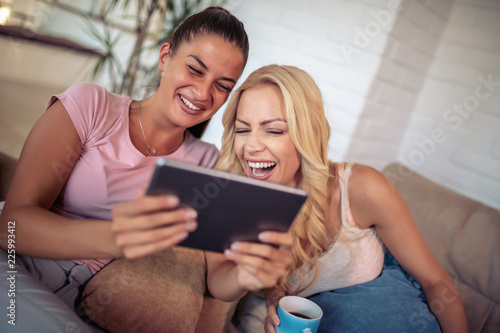 Two happy female friends using digital tablet