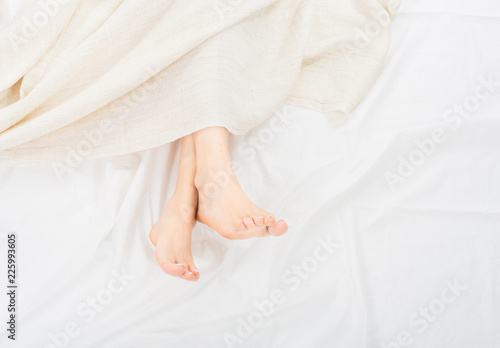 Female feet under blanket flat lay. Female beautiful feet with red pedicure on the bed. Top view on the sleeping woman legs under blanket.