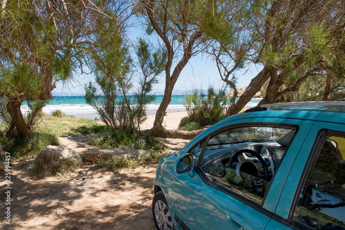 Green car parked on sand beach under the trees