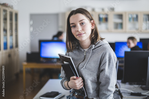 Portrait of confident high school female student with books in classroom photo