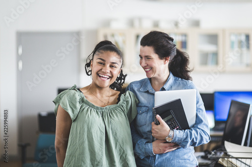 Portrait of smiling teenage student standing with teacher in computer lab at high school photo