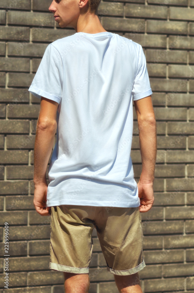 Urban template of clothes. Stylish hipster which stand on a brick wall in a blank T-shirt Urban template of clothes. Stylish hipster which stand on a brick wall in a blank T-shirt