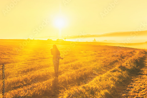 Fototapeta Naklejka Na Ścianę i Meble -  Young woman in the winter jacket with camera on the road against the background of the sunrise autumn field. Travel and tourism concept