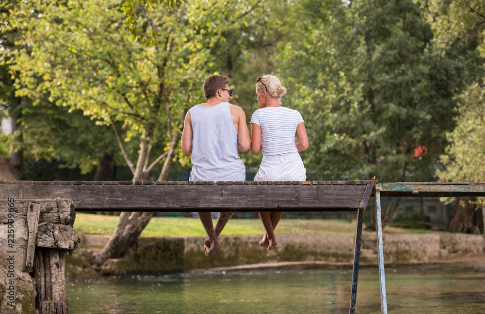 couple enjoying watermelon while sitting on the wooden bridge