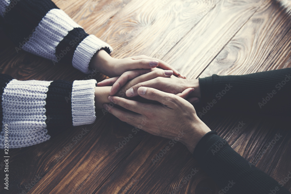 Naklejka premium man and a woman holding hands at a wooden table