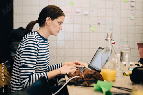 Side view of young businesswoman encrypting on laptop while sitting at desk in small office photo