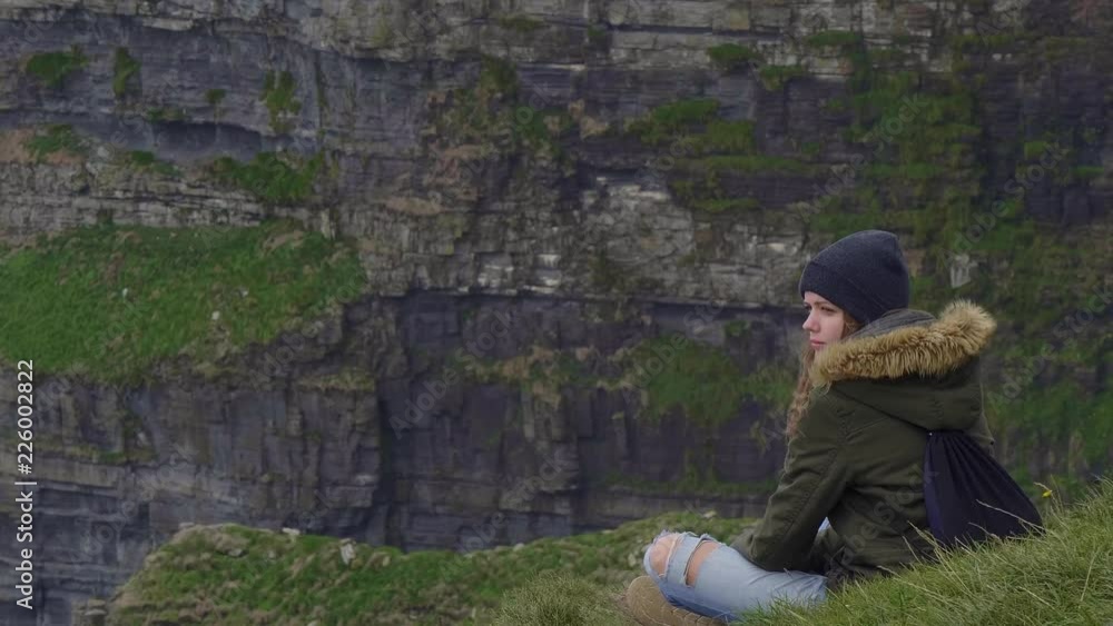 Perfect place to relax - girls sits on the top of the Cliffs of Moher Perfect place to relax - girls sits on the top of the Cliffs of Moher