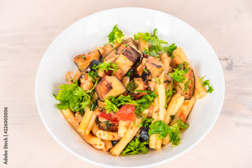 Italian food - Sicilian pasta with eggplants in a white plate on a light rustic wooden table Italian food - Sicilian pasta with eggplants in a white plate on a light rustic wooden table