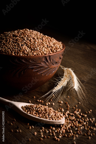 Buckwheat in a wooden bowl on a wooden background near the ears of wheat. wooden spoon with Buckwheat