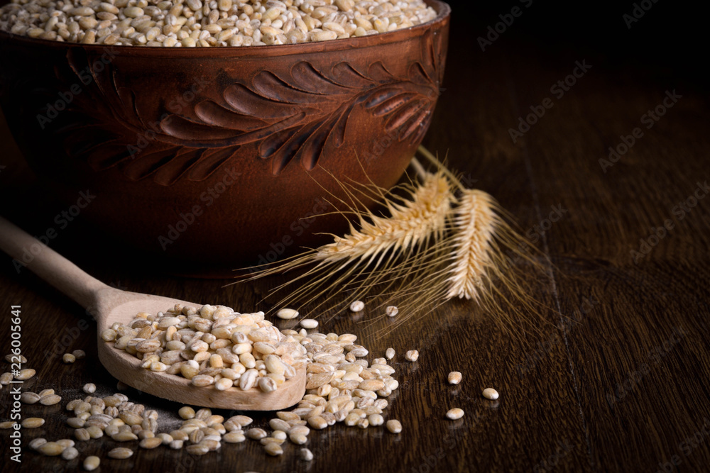 Pearl barley in a wooden bowl on a wooden background near the ears of wheat. wooden spoon with pearl barley