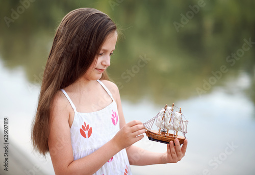 girl playing with a toy sailing ship by the river photo