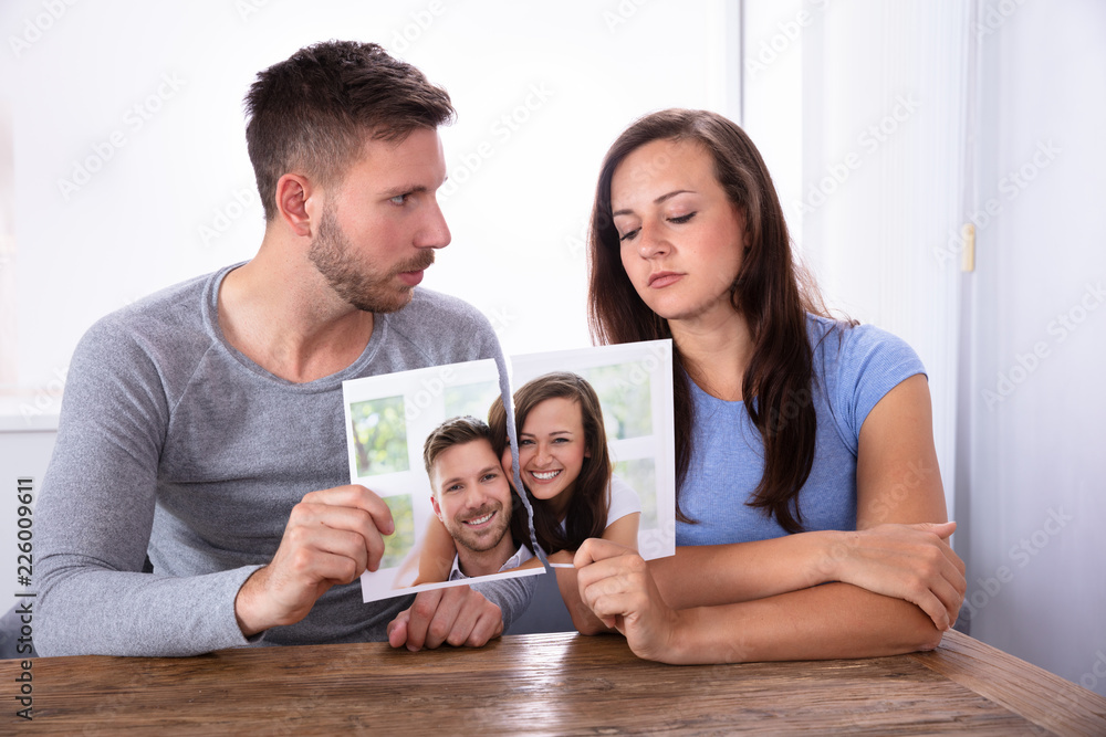 Sad Young Couple Holding Their Torn Photograph Sad Young Couple Holding Their Torn Photograph