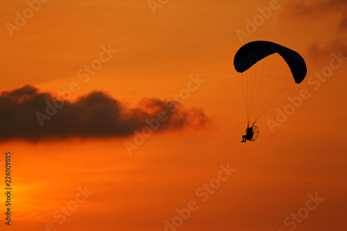 Silhouette of paramotor flying at during the sunset