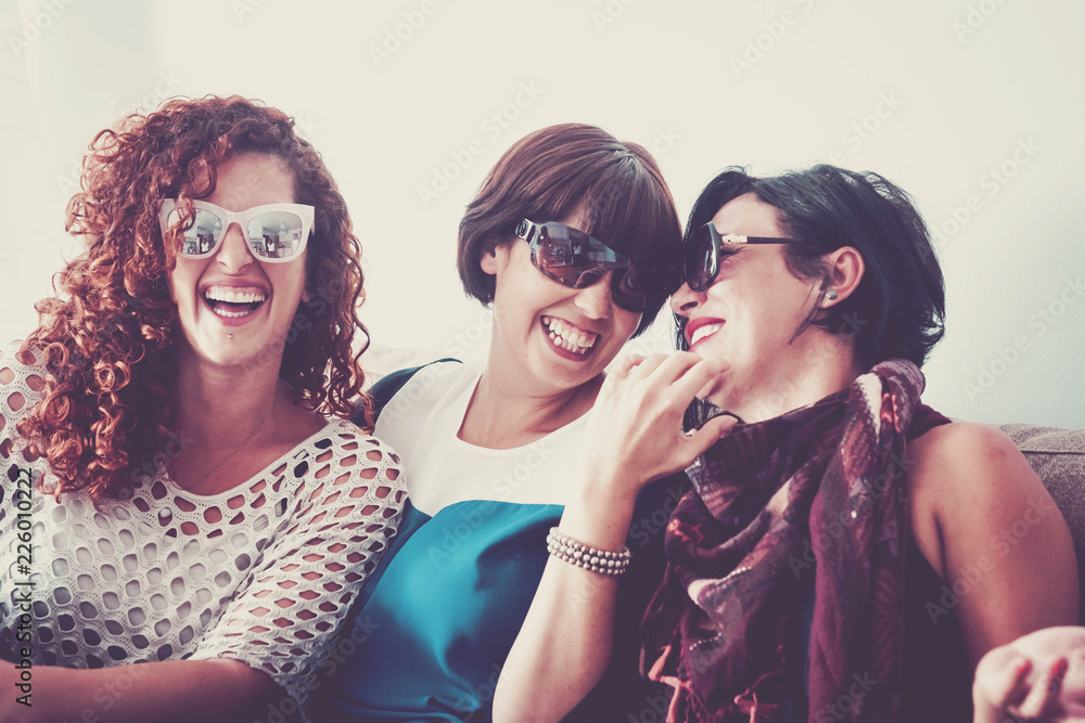 three young crazy females friends having a lot of fun at home on the sofa. all of them with sunglasses and laughi and smiles. close contact for best friendship. joy and people smiling, vintage colors