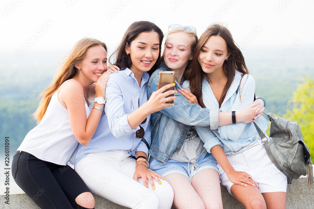 Four beautiful young women using smartphone and smiling in the Park, outdoor