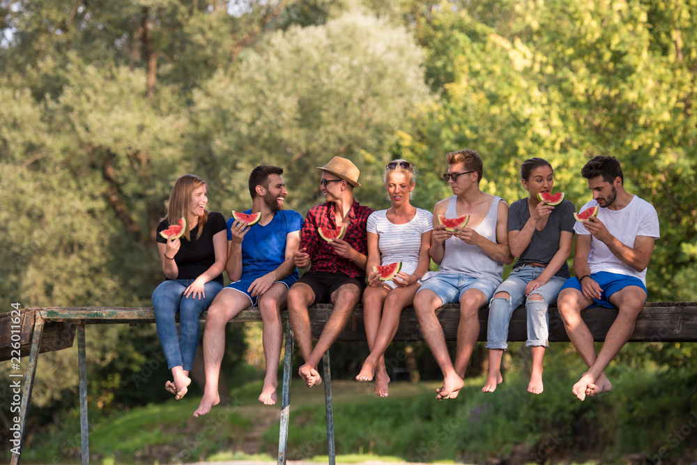 friends enjoying watermelon while sitting on the wooden bridge friends enjoying watermelon while sitting on the wooden bridge
