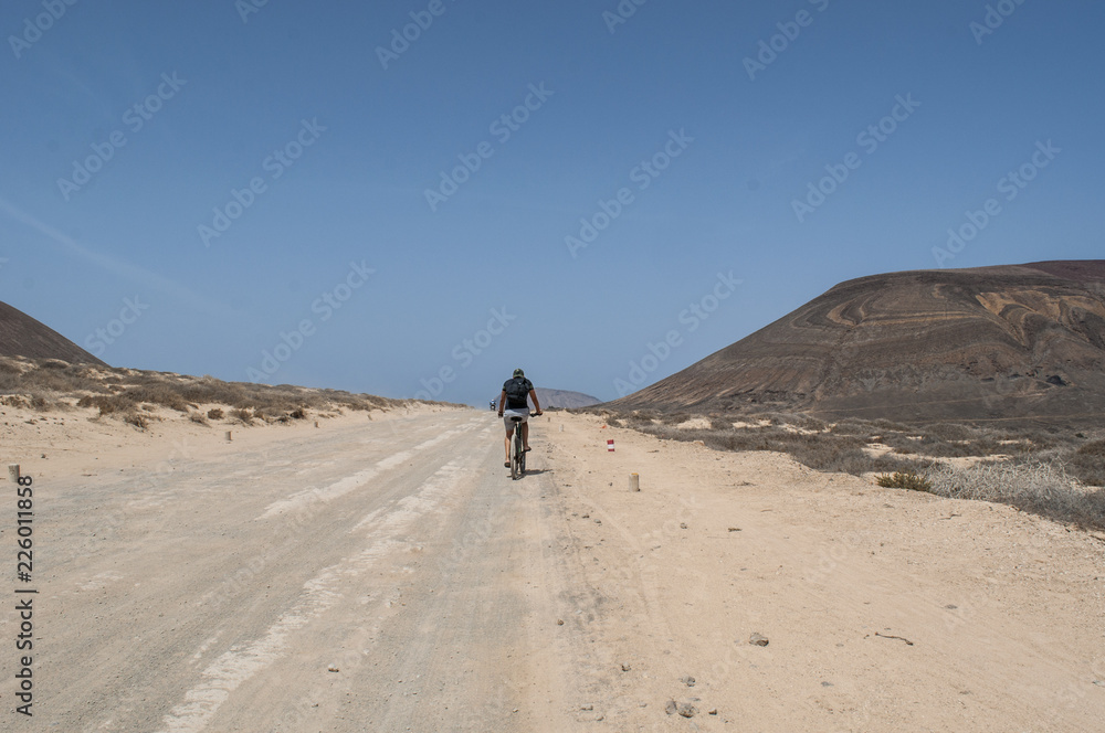 Lanzarote, isole Canarie: ragazzo di spalle in bicicletta sulla strada sterrata per la spiaggia Playa de Las Concisa sull'isola La Graciosa