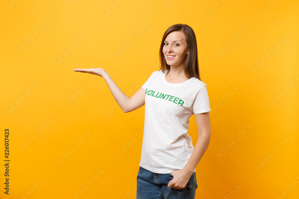 Portrait of happy smiling satisfied woman in white t-shirt with written inscription green title volunteer isolated on yellow background. Voluntary free assistance help, charity grace work concept. Portrait of happy smiling satisfied woman in white t-shirt with written inscription green title volunteer isolated on yellow background. Voluntary free assistance help, charity grace work concept.
