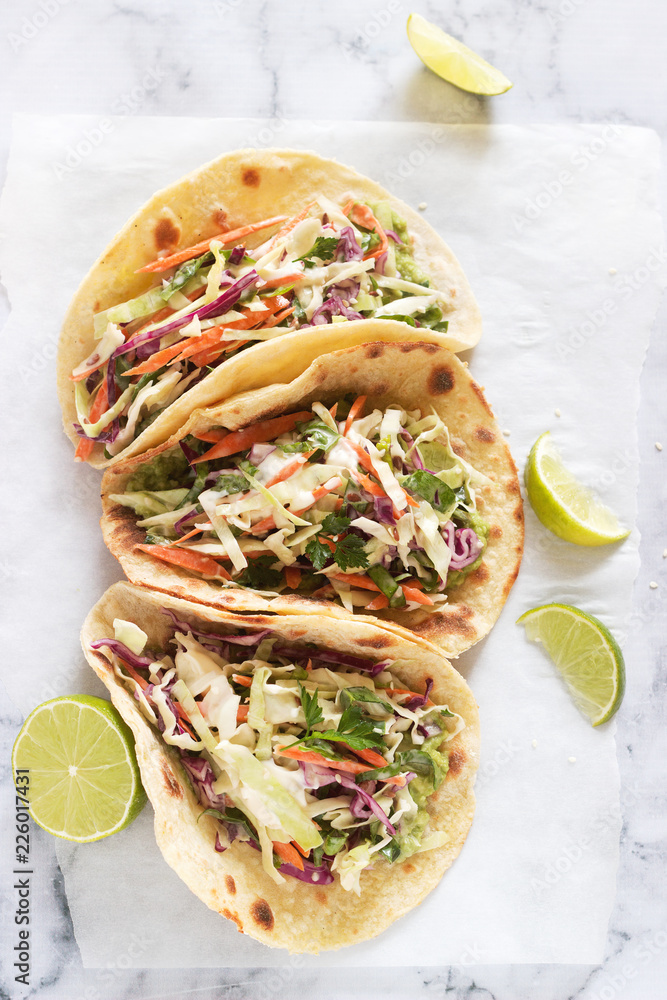 Tacos with guacamole and coleslaw served with lime slices on a light background.