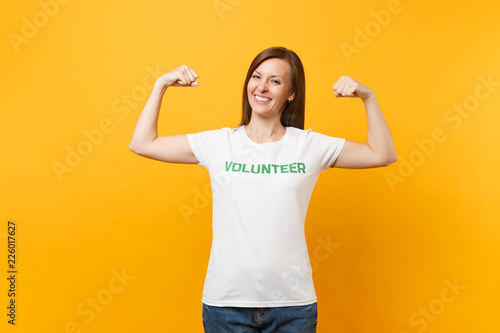 Portrait of happy smiling satisfied woman in white t-shirt with written inscription green title volunteer isolated on yellow background. Voluntary free assistance help, charity grace work concept.