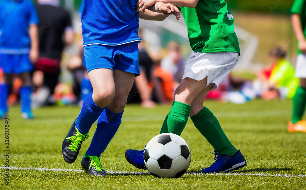 Boys kicking football match on the sports field. Kids soccer teams compete in the school soccer tournament. Children in blue and green sport jersey and football cleats.